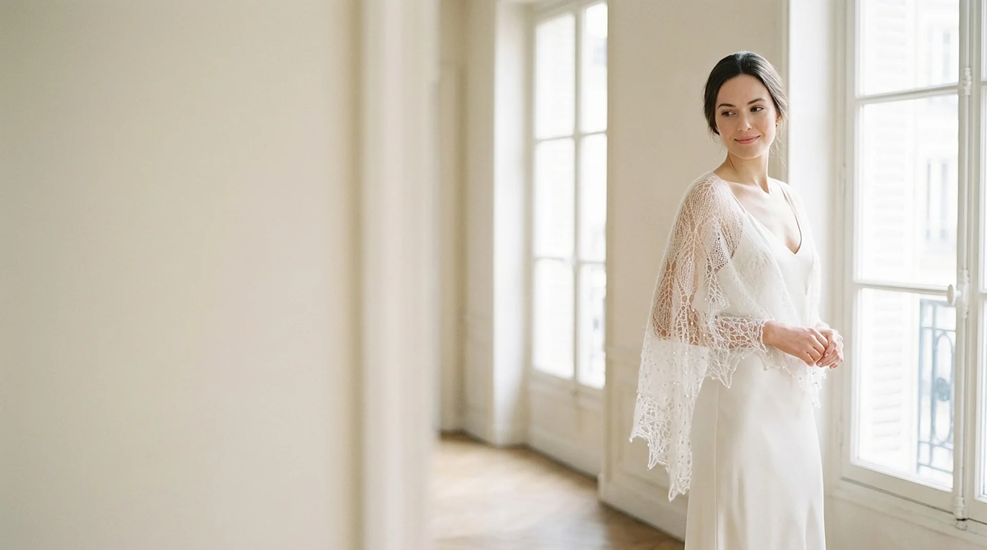Mariée près d'une fenêtre parisienne, châle de dentelle blanc tricoté main sur les épaules